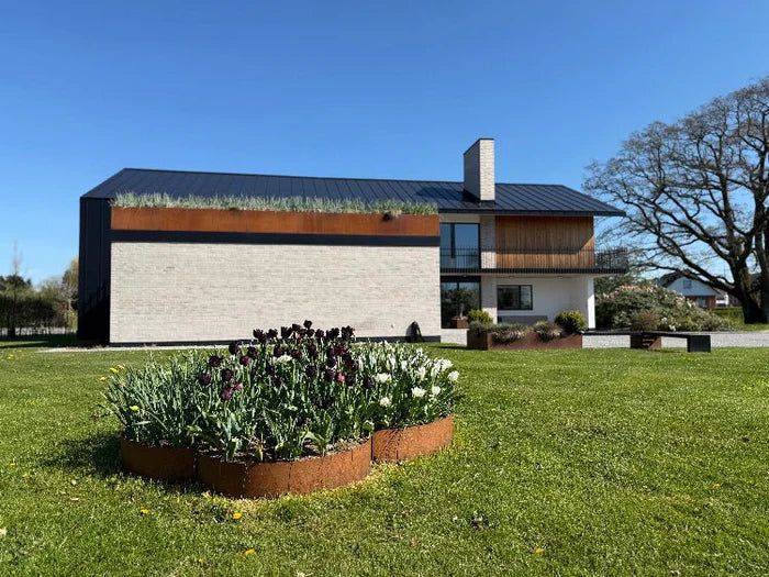 Runde Beeteinfassung aus Cortenstahl um einen Fahnenmast mit Blumenbeet