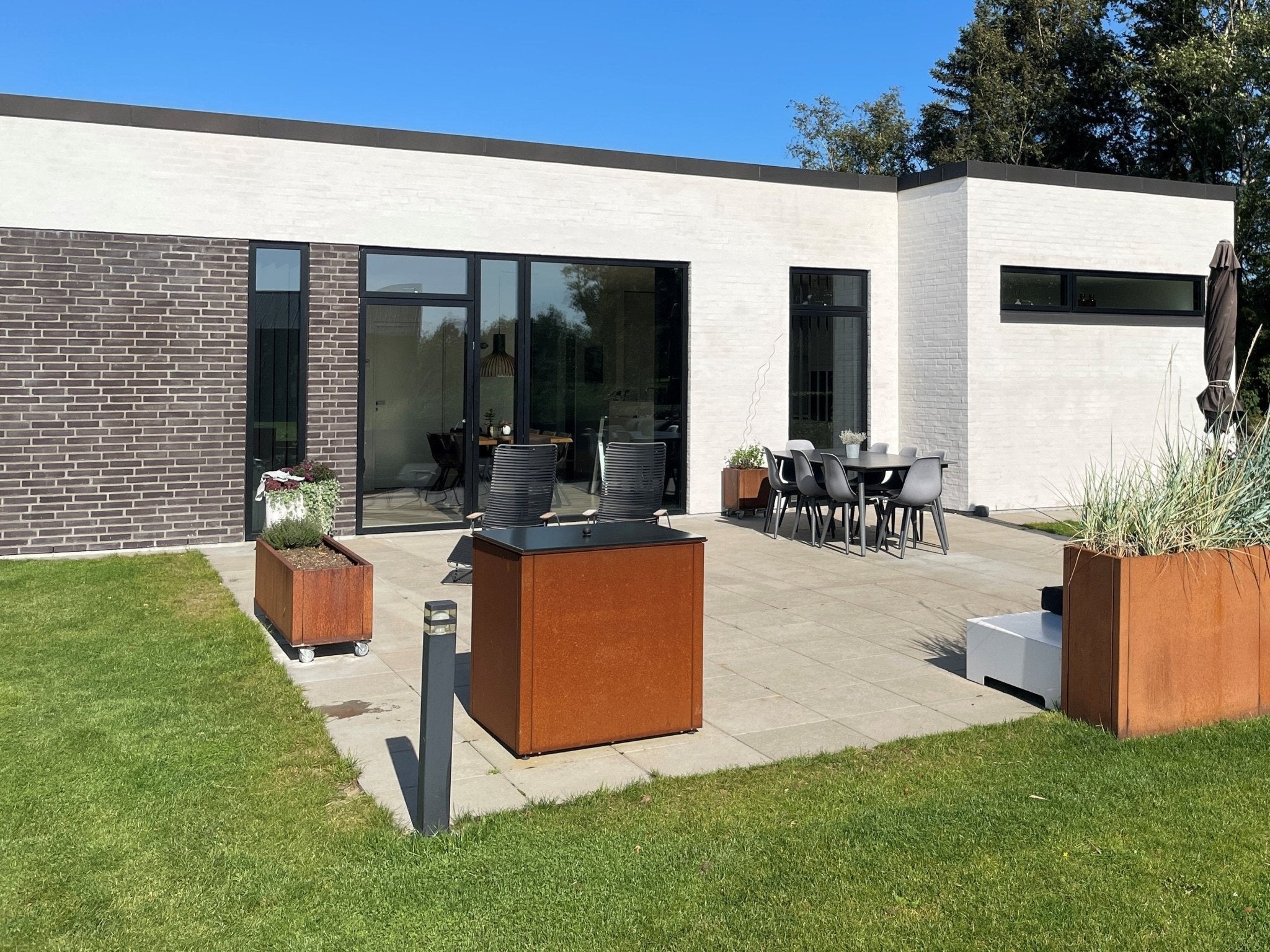 byJEMA Feuerstelle aus Cortenstahl auf moderner Terrasse mit passenden Pflanzkübeln – stilvolle Outdoor-Feuerstelle im architektonischen Garten
