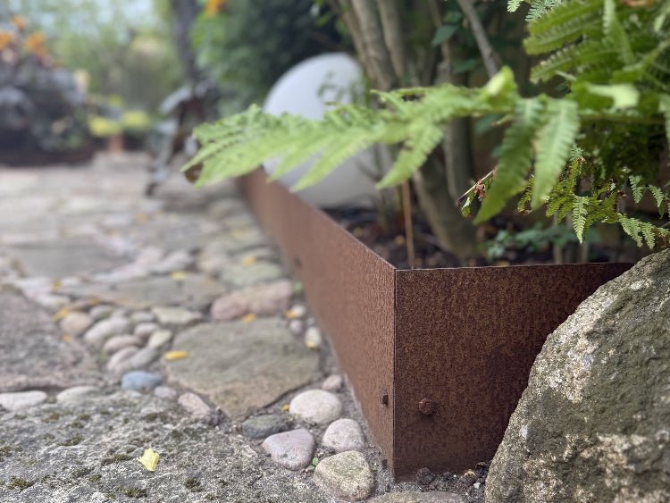 Rasenkante aus Cortenstahl entlang eines Steinwegs – dekorative und funktionale Beetabgrenzung