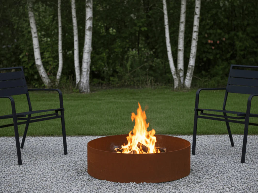 Runde Cortenstahl Feuerring im modernen Garten mit Kiesflaeche und Sitzmoebeln