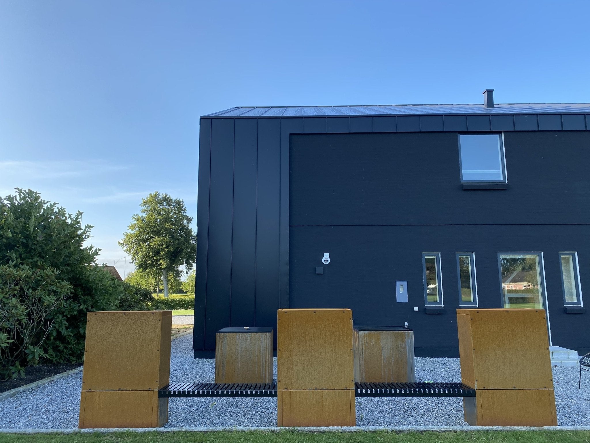 Cortenstahl Holzlager mit durchgehender Sitzbank als modernes Gartenmöbel