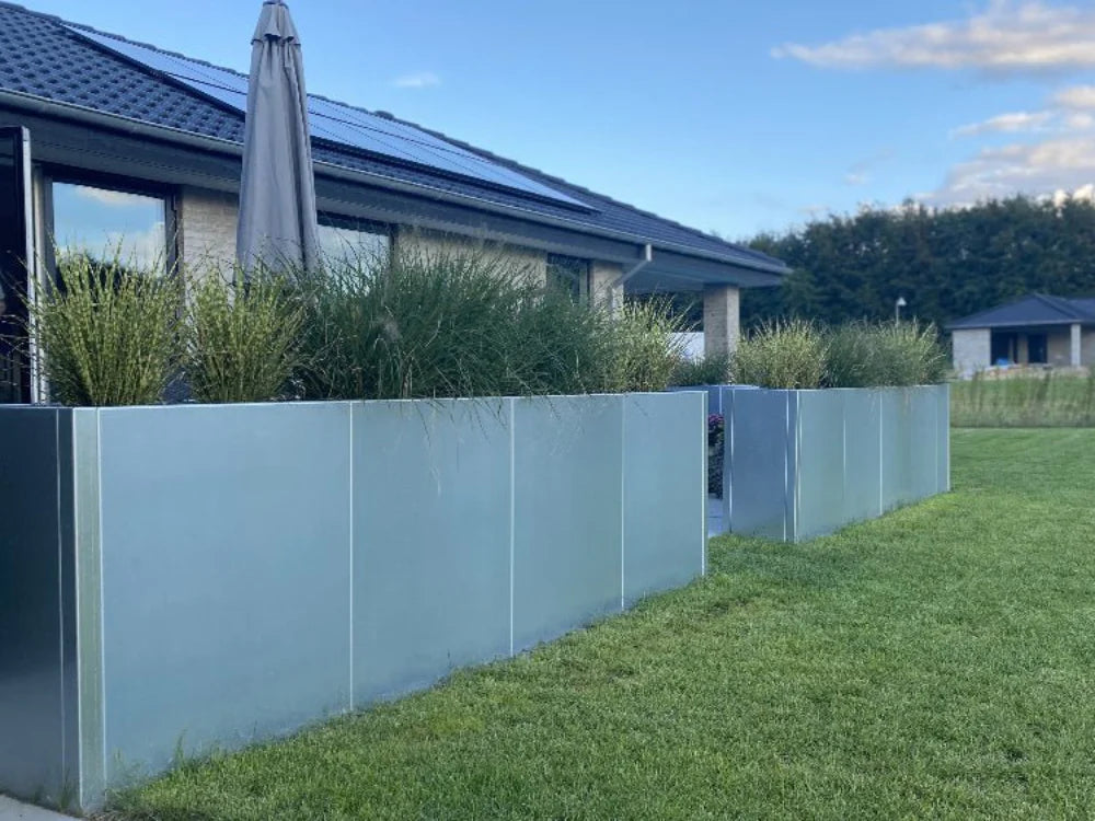 Reihe von Pflanzkübeln aus verzinktem Stahl entlang einer Rasenfläche im Garten