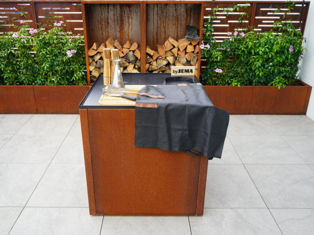 CUBY Outdoor-Küchentisch aus Cortenstahl vor Holzlager