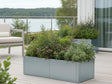 CUBY niedriger Pflanzkübel aus verzinktem Stahl mit grünen Pflanzen auf Terrasse mit Ausblick
