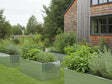 Hochbeete aus verzinktem Stahl mit Pflanzen entlang der Hausfassade im Naturgarten