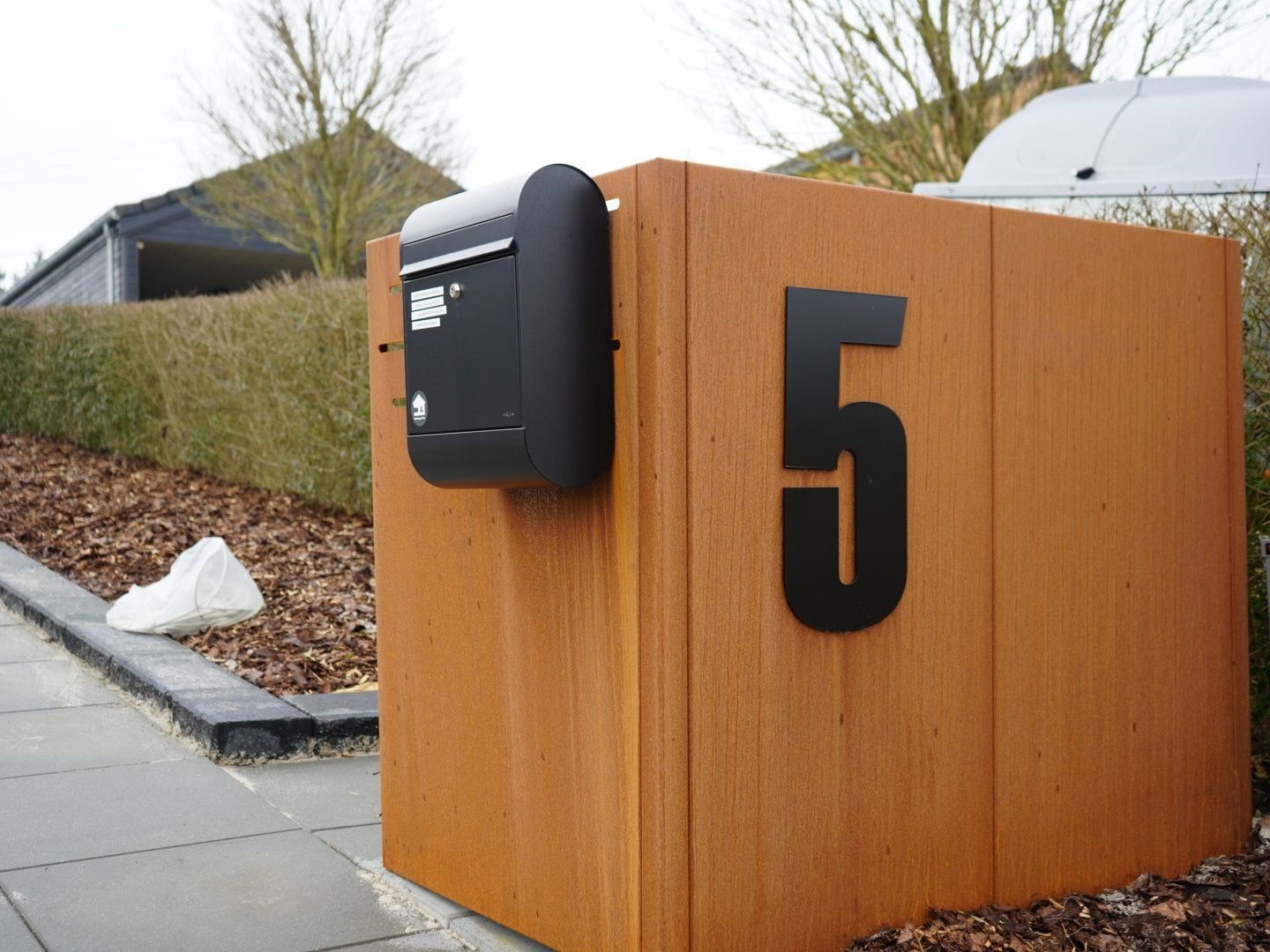 Detailansicht einer Mülltonnenbox aus Cortenstahl mit aufgesetzter Hausnummer und Briefkasten