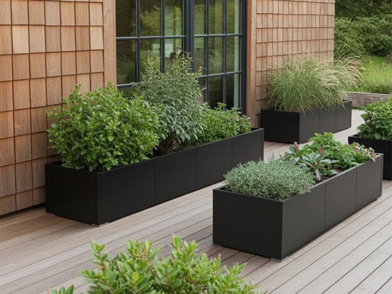 Pflanzkästen aus schwarzem Stahl mit Stauden und Ziergräsern entlang einer Holzfassade