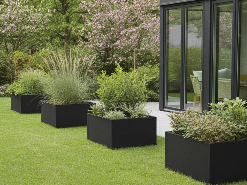 Pflanzkästen aus schwarzem Stahl mit Ziergräsern und Sträuchern auf Rasenfläche