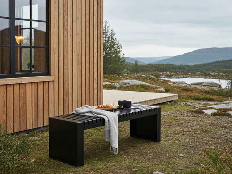 U-Bank aus schwarzem Stahl vor nordischem Holzhaus